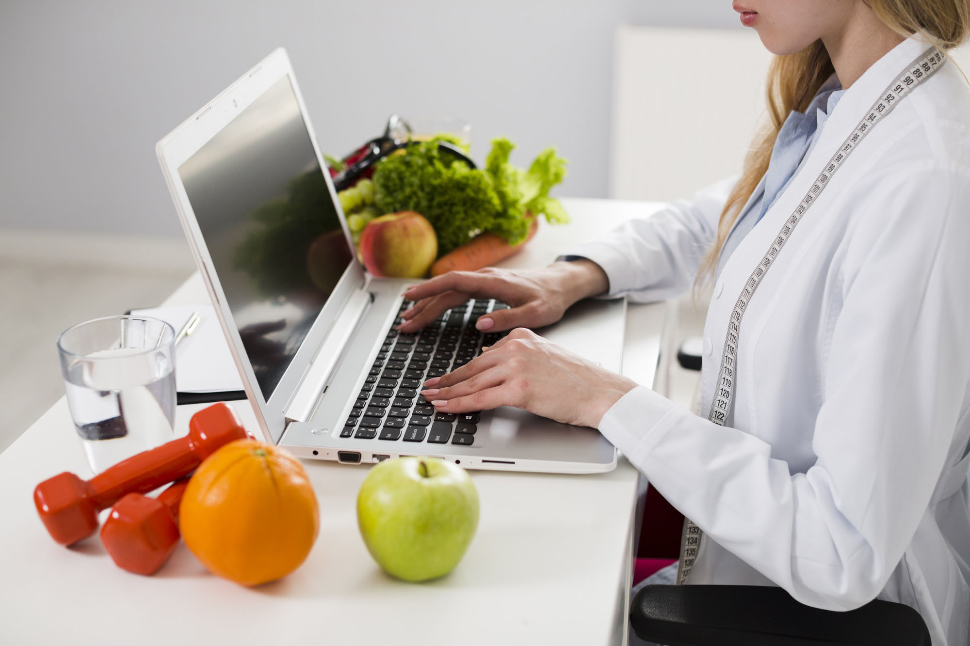 Nutricionista escribiendo en una computadora con frutas y verduras.